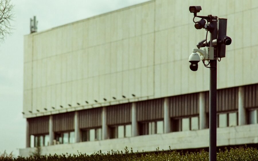 Black and white photograph of multiple surveillance cameras mounted on a pole in front of a concrete building; illustrative, not footage from the IACP conference or an identified Flock device